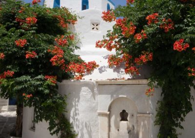 Το κυκλαδίτικο εκκλησάκι της Αγίας Τριάδας και η ιστορική κρήνη του Μαυρογέννη στην Παροικιά, απέναντι από την είσοδο του ξενοδοχείου